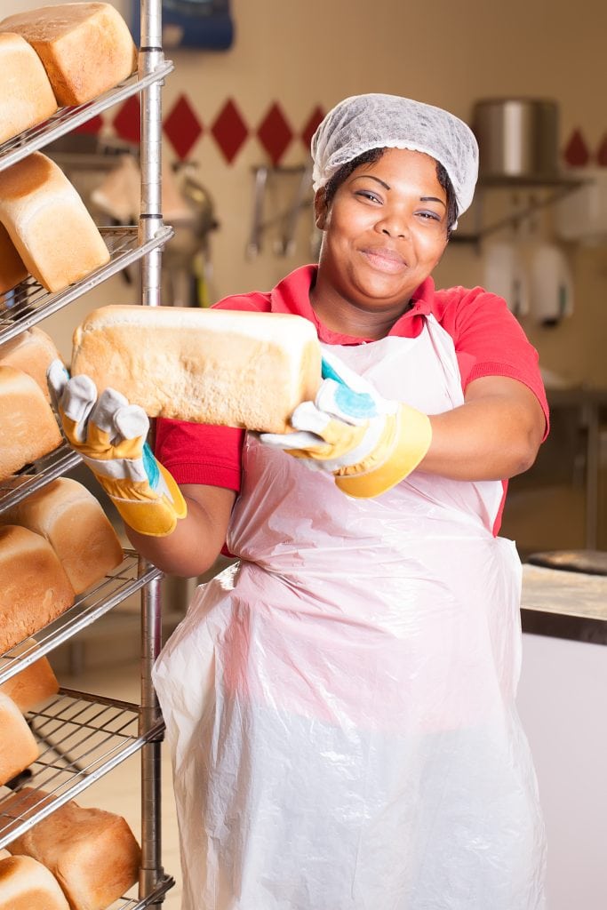 young african woman wearing heat-protected gloves preparing fresh bread loaves to be cooled on the rack